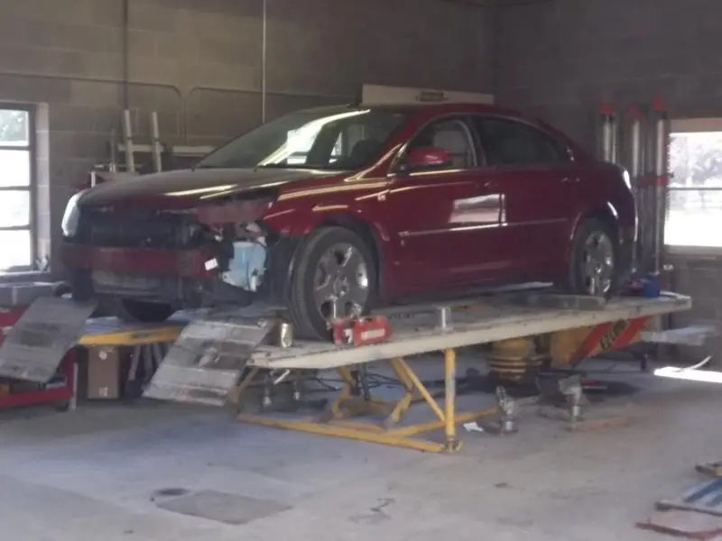 Red sedan with front end collision damage on the frame rack