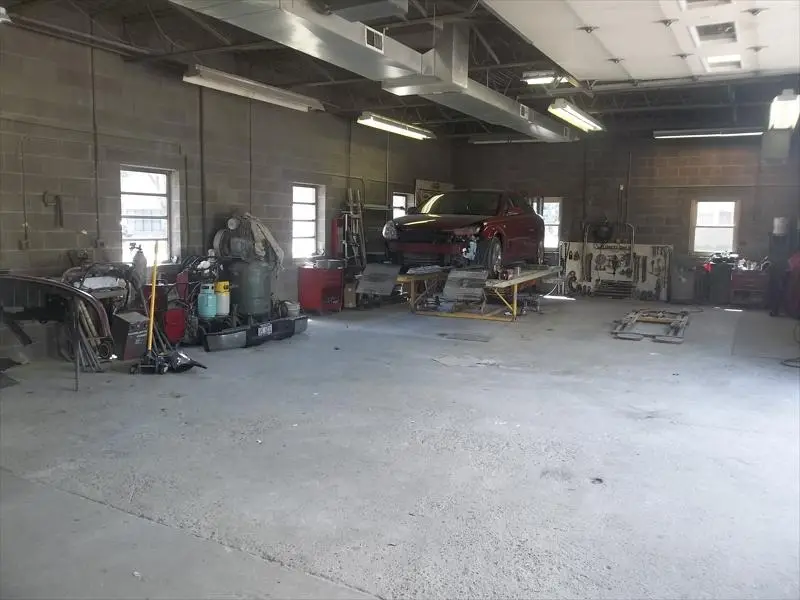 Repair bay with a red sedan on the frame rack and equipment along the wall
